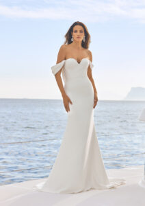Aubrey by Pronovias. A glamorous fit and flare, off the shoulder, crepe wedding dress. It is available in Belladonna Bridal, Galway